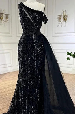 Black evening gown with a sheer overlay on a mannequin against a white wall2026 glitter sparkling diamonds, side shoulder off the shoulder, mermaid, train, old-money classy elegant dubai style, saudi arabic, sleeveless, elliesaab, prom, wedding guest, bridesmaid, mother of the bride, christmas, luxury, celebrity, expensive cheap, vintage, real photos, high-end, chooseone, viral, where to buy, now, shop, store, miss universe, best, number one top, glamorous, sexy, simple, haul, shein, dance, formal, give me 